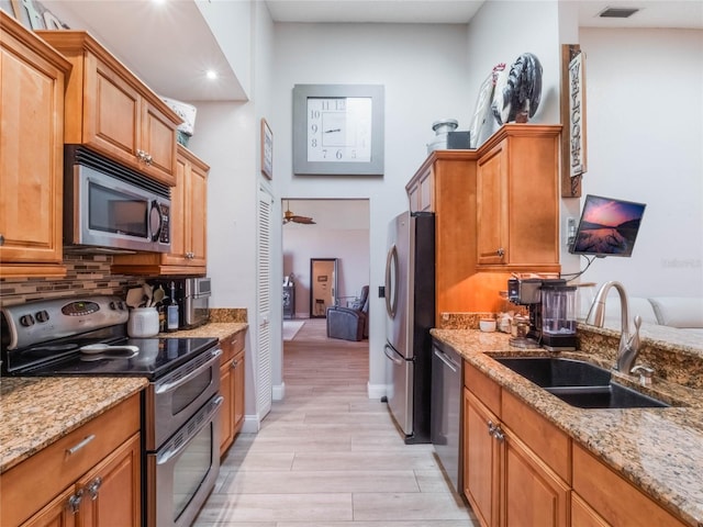 kitchen with light stone countertops, appliances with stainless steel finishes, sink, and decorative backsplash