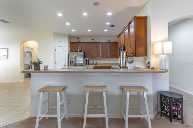 kitchen with a kitchen bar, stainless steel fridge, kitchen peninsula, and light tile patterned floors