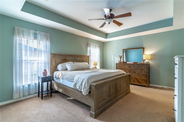 carpeted bedroom with ceiling fan and a tray ceiling