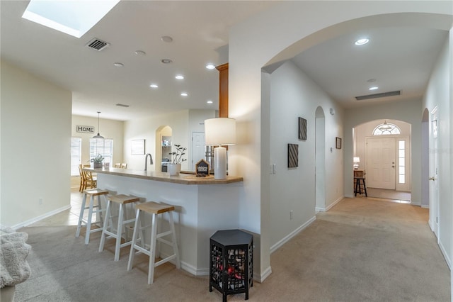 kitchen featuring light colored carpet, a kitchen breakfast bar, kitchen peninsula, and decorative light fixtures