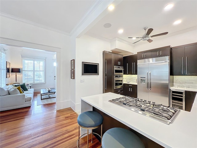 kitchen with a breakfast bar, appliances with stainless steel finishes, wine cooler, light hardwood / wood-style floors, and ornamental molding