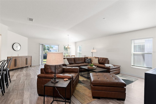 living room with a wealth of natural light, a textured ceiling, a chandelier, and light hardwood / wood-style floors