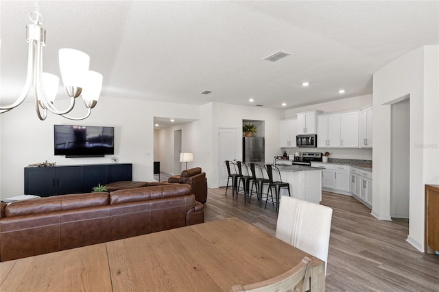 living room with sink, light hardwood / wood-style floors, a textured ceiling, and a notable chandelier