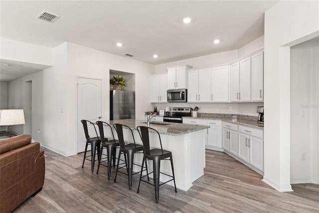 kitchen with a breakfast bar area, a center island with sink, stone counters, stainless steel appliances, and white cabinets