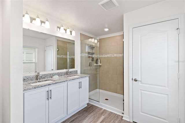 bathroom with vanity, hardwood / wood-style flooring, a textured ceiling, and tiled shower