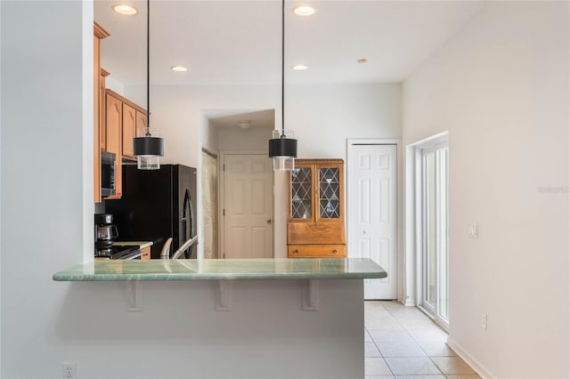 kitchen with black fridge, kitchen peninsula, hanging light fixtures, and a breakfast bar area