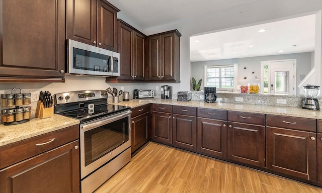 kitchen featuring a textured ceiling, dark brown cabinets, light wood-type flooring, appliances with stainless steel finishes, and light stone countertops