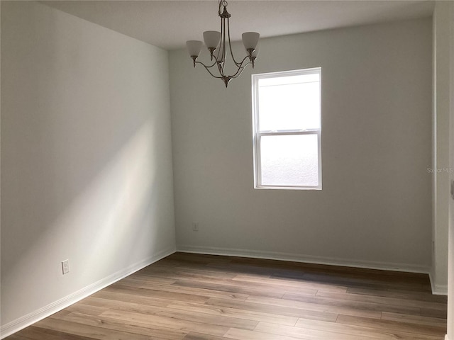 spare room with an inviting chandelier, light wood-style flooring, and baseboards