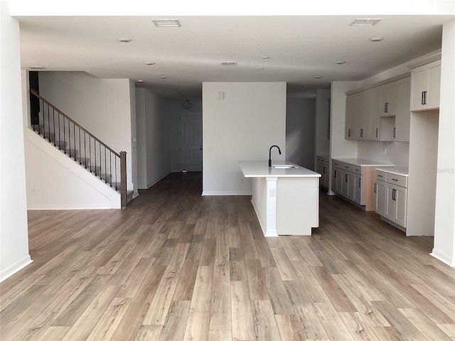 kitchen featuring baseboards, visible vents, light countertops, light wood-style floors, and a sink