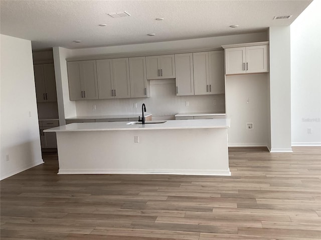 kitchen with gray cabinetry, a sink, visible vents, light wood-style floors, and a center island with sink