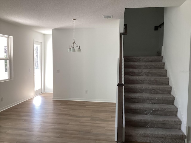 stairway with visible vents, a textured ceiling, baseboards, and wood finished floors