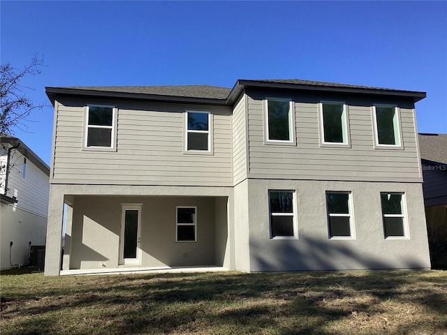 back of property with a lawn and stucco siding