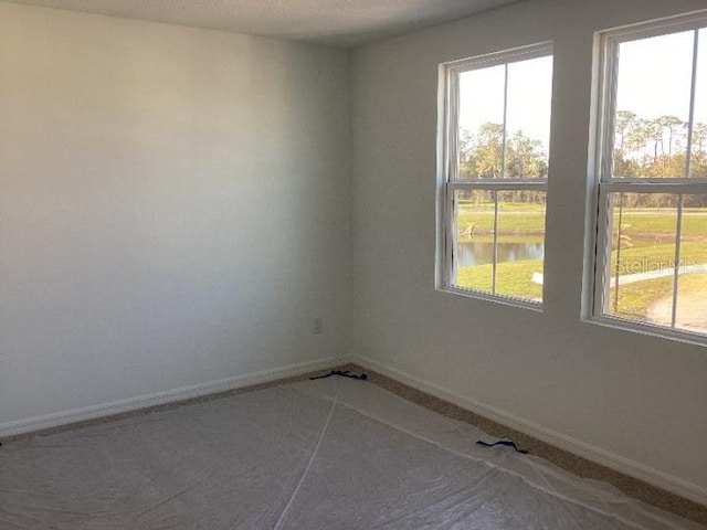 empty room featuring a water view and baseboards