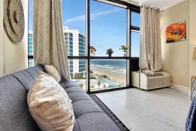 living room with expansive windows, a water view, a beach view, and a wall unit AC