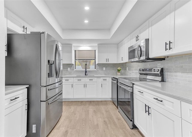 kitchen with appliances with stainless steel finishes, white cabinetry, sink, light hardwood / wood-style floors, and a tray ceiling