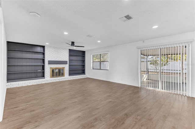 unfurnished living room featuring built in features, ceiling fan, a textured ceiling, a brick fireplace, and light wood-type flooring