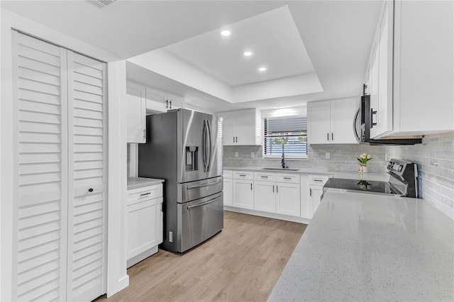 kitchen with appliances with stainless steel finishes, tasteful backsplash, white cabinetry, a raised ceiling, and light wood-type flooring