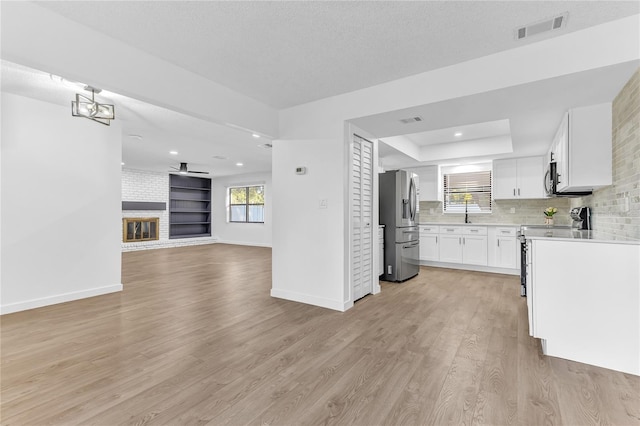 kitchen with white cabinetry, a brick fireplace, light hardwood / wood-style flooring, stainless steel appliances, and backsplash