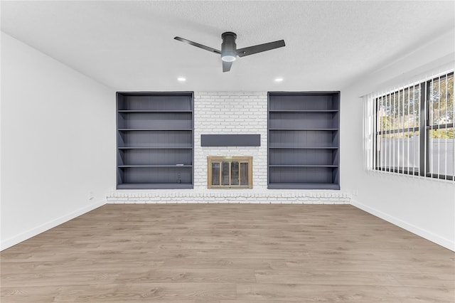 unfurnished living room featuring built in shelves, a fireplace, hardwood / wood-style floors, and a textured ceiling