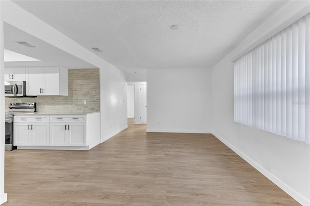 kitchen featuring light hardwood / wood-style flooring, backsplash, stainless steel appliances, a textured ceiling, and white cabinets