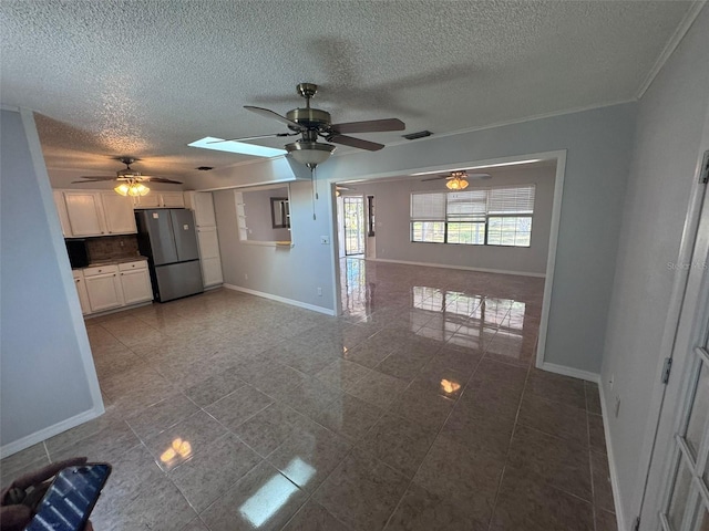 unfurnished living room with ceiling fan, a skylight, and a textured ceiling