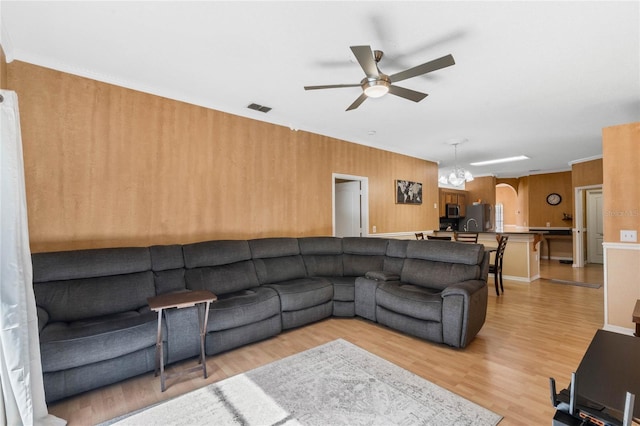 living room with ceiling fan with notable chandelier and light hardwood / wood-style floors