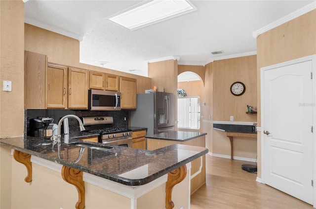 kitchen featuring a kitchen breakfast bar, dark stone counters, kitchen peninsula, stainless steel appliances, and crown molding