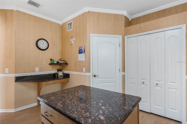 kitchen featuring built in desk, light wood-type flooring, dark stone counters, ornamental molding, and a textured ceiling