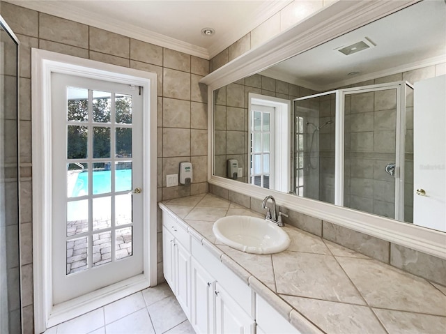 bathroom featuring tile walls, vanity, a shower with door, crown molding, and tile patterned floors