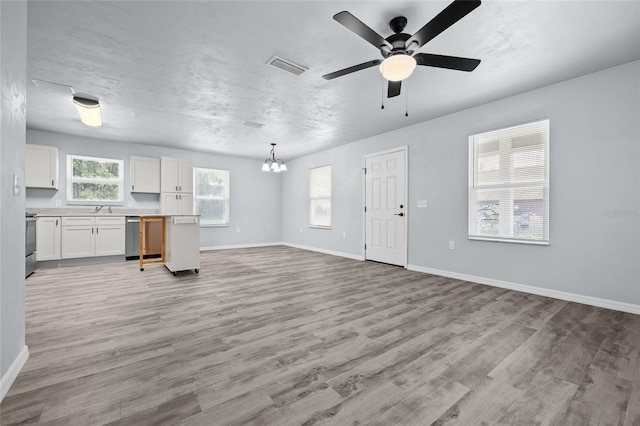 unfurnished living room featuring sink, ceiling fan with notable chandelier, light hardwood / wood-style floors, and a textured ceiling