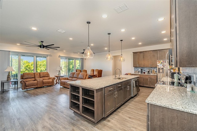 kitchen featuring sink, hanging light fixtures, a center island with sink, appliances with stainless steel finishes, and light stone countertops