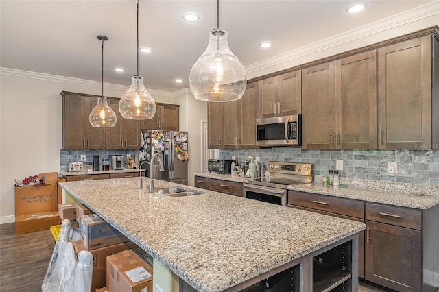 kitchen with sink, hanging light fixtures, appliances with stainless steel finishes, light stone countertops, and a kitchen island with sink