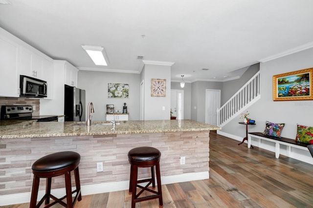 kitchen featuring appliances with stainless steel finishes, a breakfast bar, sink, white cabinets, and light stone countertops