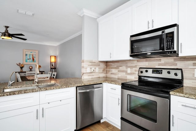 kitchen featuring white cabinetry, crown molding, kitchen peninsula, stainless steel appliances, and light stone countertops