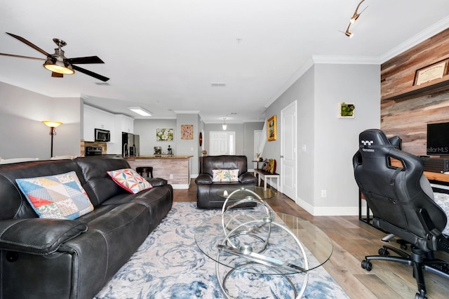 living room featuring crown molding, ceiling fan, wooden walls, and light hardwood / wood-style flooring