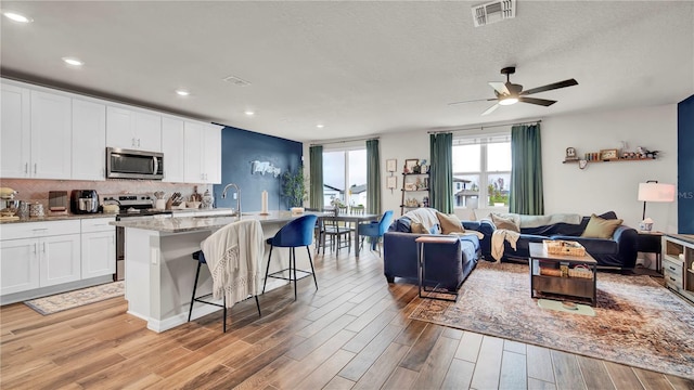 kitchen featuring white cabinetry, an island with sink, a breakfast bar area, stainless steel appliances, and light hardwood / wood-style flooring