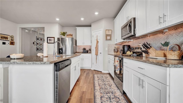 kitchen featuring sink, white cabinets, stainless steel appliances, a center island with sink, and light hardwood / wood-style flooring