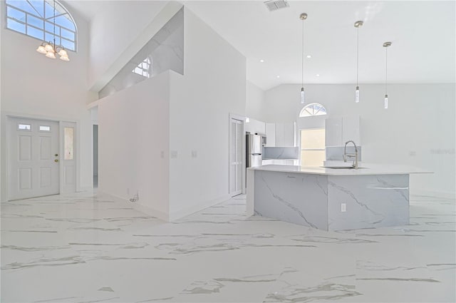 kitchen featuring sink, stainless steel fridge, white cabinets, a center island with sink, and decorative light fixtures