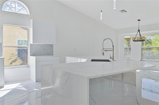 kitchen featuring white cabinetry, a kitchen island with sink, light stone counters, and decorative light fixtures