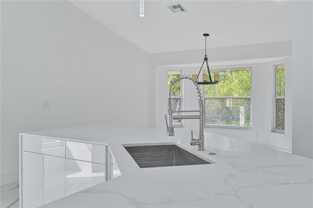 kitchen featuring light stone countertops, sink, white cabinets, and decorative light fixtures