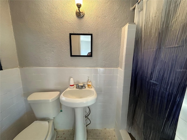 bathroom with walk in shower, toilet, and tile walls