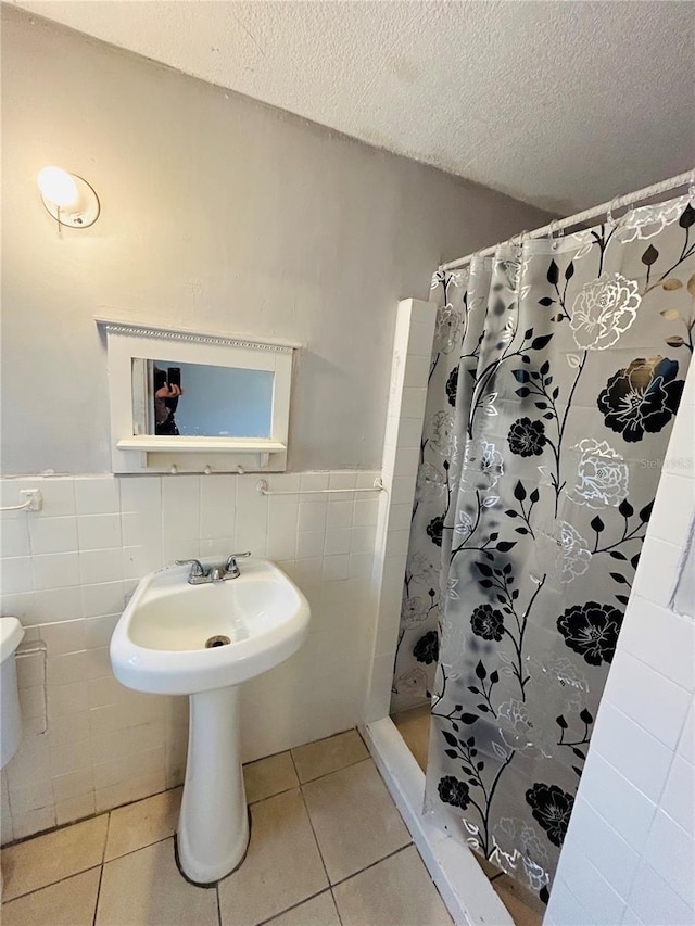 bathroom with sink, tile walls, a textured ceiling, curtained shower, and tile patterned floors