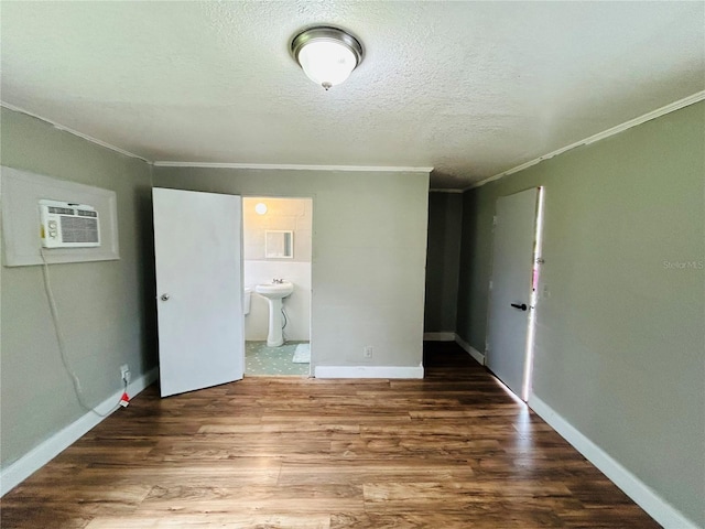 unfurnished bedroom featuring ensuite bathroom, crown molding, a textured ceiling, a wall unit AC, and hardwood / wood-style floors