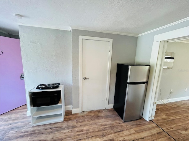 kitchen with stainless steel refrigerator, ornamental molding, hardwood / wood-style floors, and a textured ceiling