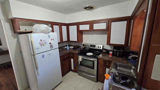 kitchen with light tile patterned flooring, sink, white fridge, electric range, and a textured ceiling