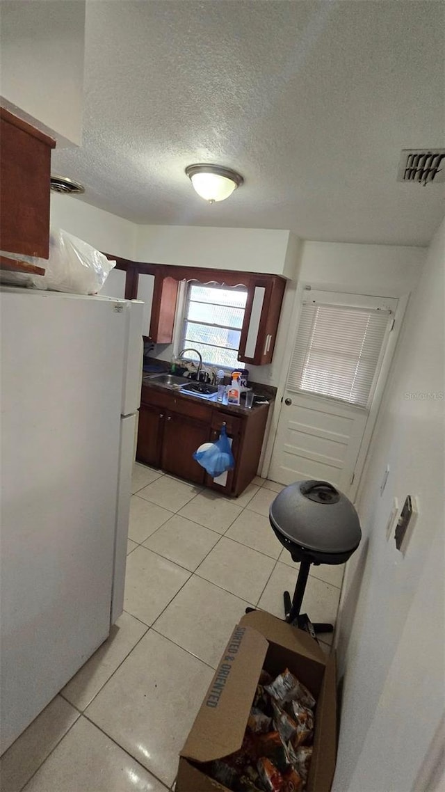 kitchen with sink, light tile patterned floors, a textured ceiling, and white refrigerator