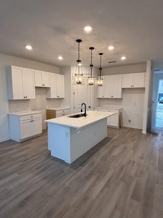 kitchen with pendant lighting, sink, white cabinetry, wood-type flooring, and a center island with sink