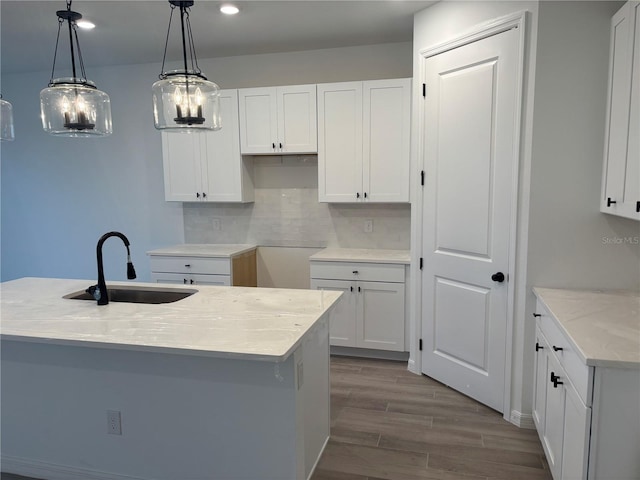 kitchen with white cabinetry, sink, hanging light fixtures, light stone countertops, and a center island with sink