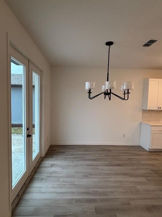 unfurnished dining area with a notable chandelier, light hardwood / wood-style floors, and french doors