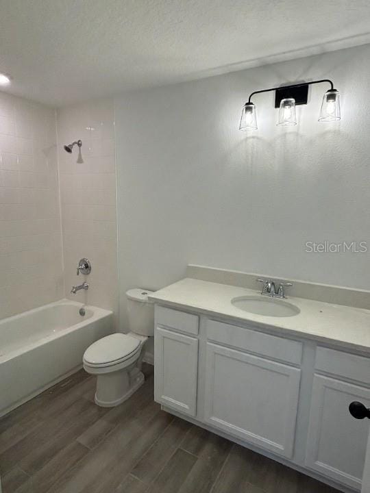 full bathroom with toilet, tiled shower / bath, a textured ceiling, vanity, and hardwood / wood-style floors